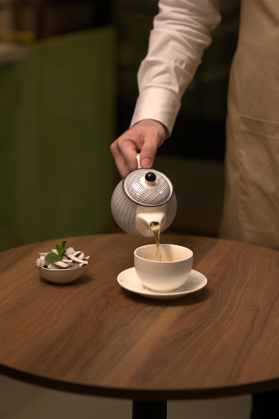 A server pouring tea beside a coconut dessert at a walnut table