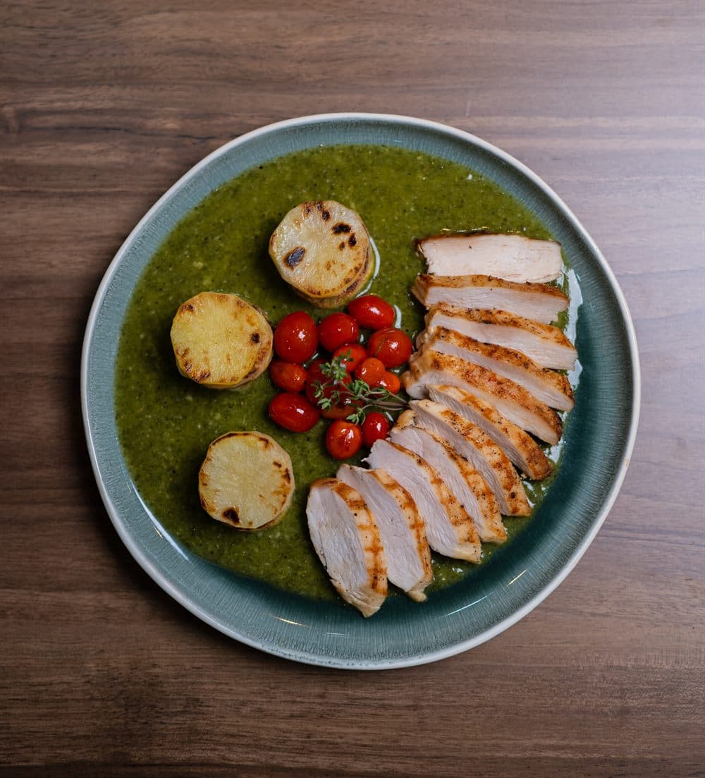 Poulet Grillé — sliced herb chicken over a green herb sauce with roasted potatoes and vine tomatoes